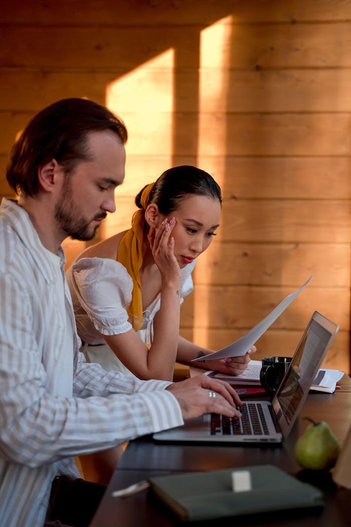 services-01 Two adults collaborating on a project using a laptop and papers in a sunlit wooden room.